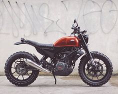 a red and black motorcycle parked in front of a wall with graffiti written on it