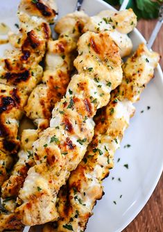 chicken skewers are served on a white plate with parsley garnish