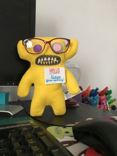 a yellow stuffed animal with glasses on it's head sitting in front of a computer keyboard