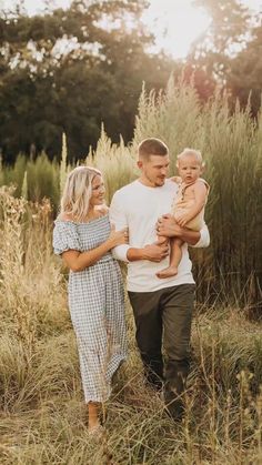 a man, woman and child walking through tall grass with the sun shining on them