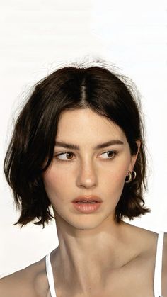 a close up of a person wearing a white shirt and necklace with an earring