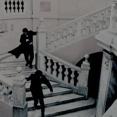 black and white photograph of two people walking up stairs in a building with marble balconies