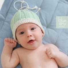 a baby wearing a knitted hat laying on top of a blue blanket with white trim