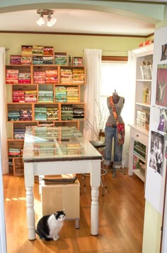 a cat sitting on the floor in front of a table with bookshelves behind it