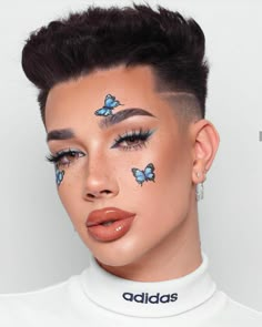 a woman with blue butterflies painted on her face and eyebrows, wearing white shirt and silver earrings