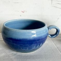 a large blue bowl sitting on top of a white cloth covered table next to a wall