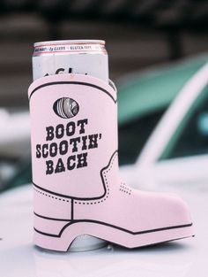 a pink boot shaped can cooler sitting on top of a white car with the words boot scootin'back printed on it