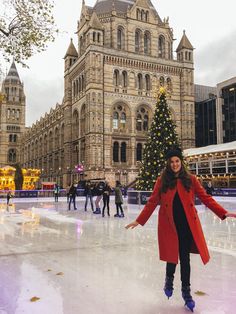 a woman standing on an ice rink in front of a large building with a christmas tree