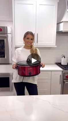 a woman standing in a kitchen holding a red crock pot