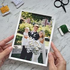 a couple holding a bouquet of daisies in front of their wedding photo on a marble table