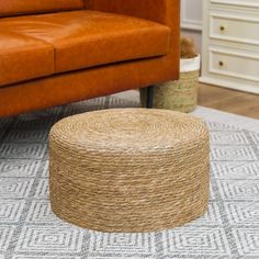 a living room with a brown leather couch and round jute ottoman on the floor