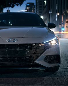 the front end of a silver car on a city street at night