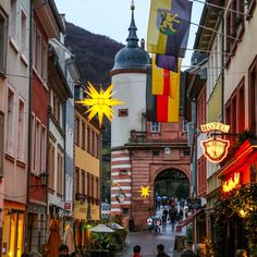 people are walking down an alley way with flags hanging from the buildings on either side