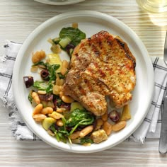 a white plate topped with meat, beans and veggies next to a glass of wine