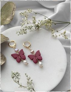 two pink and gold butterfly earrings on a white plate with flowers in the back ground