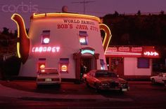 an old fashioned diner with neon lights on the side of it's building and cars parked in front