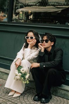 a man and woman sitting on the ground next to each other with sunglasses on their faces