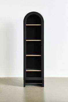 a tall black cabinet with gold trim on the bottom and shelves below it, in front of a white wall