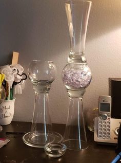 two glass vases sitting on top of a table next to a phone and flowers