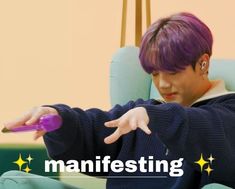 a man with purple hair sitting in a chair pointing at something on his finger and the words manifesting above him