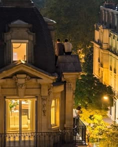 two people are sitting on the roof of a building at night, looking out into the city