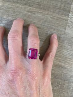 This stunning ring boasts a 7.6 carat emerald cut cultured ruby set in a beautiful sterling silver band. The vibrant pink hue of the main stone is complemented by the simplicity of the metal, creating a timeless and elegant piece of jewelry. The ring is a size 6 and perfect for those looking for a unique and eye-catching statement ring. Pink Emerald Cut Ruby Ring In Fine Jewelry, Emerald Cut Pink Ruby Ring In Fine Jewelry Style, Luxury Emerald-cut Ruby Ring, Ruby Emerald Ring, Pink Ruby Ring With Emerald Cut Center Stone, Ruby Ring With Rectangular Stone For Anniversary, Pink Gemstones With Prong Setting For Formal Occasions, Pink Emerald Cut Sterling Silver Ring, Gia Certified Emerald Cut Ruby Ring