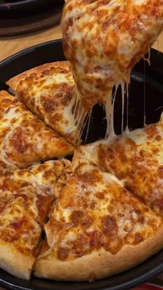 a person taking a slice of cheese pizza from a black pan on a wooden table