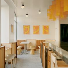 an empty restaurant with yellow and orange paintings on the wall, tables and stools