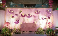 a pink couch sitting in front of a wall with flowers and flamingos on it