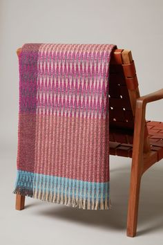 a pink and blue blanket sitting on top of a wooden bench next to a chair