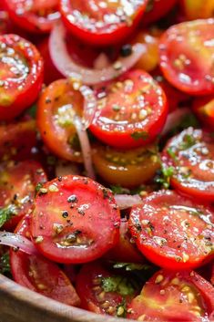 a wooden bowl filled with lots of sliced tomatoes and green stuff on top of it