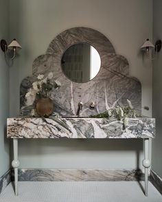 a bathroom with marble counter top and round mirror on the wall, along with two sconces