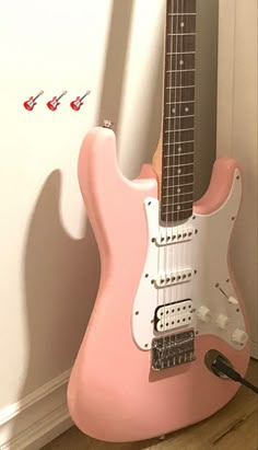 a pink guitar sitting on top of a hard wood floor next to a white wall