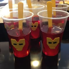 plastic cups filled with red liquid and yellow sticks sticking out of the lids, sitting on a table