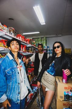 three people standing in a store with boxes and cans on the shelves, one woman is holding a shopping cart