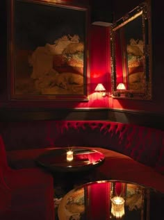 two red couches with candles lit on them in a dimly lit room next to paintings