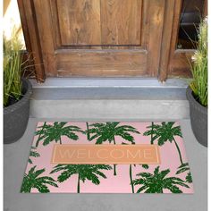 a welcome mat with palm trees in front of a wooden door and potted plants