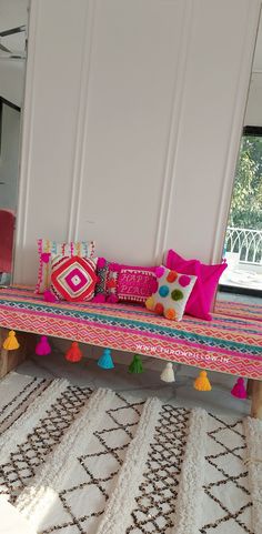 a pink bench with colorful pillows and pom - poms on it