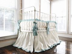 a white crib with blue ruffles in front of a window and wooden floor