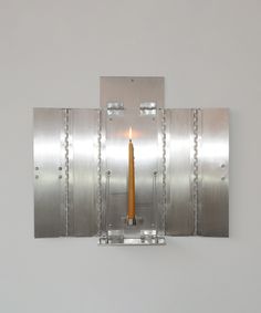 a candle that is sitting in the middle of a metal wall mounted light fixture on a white wall