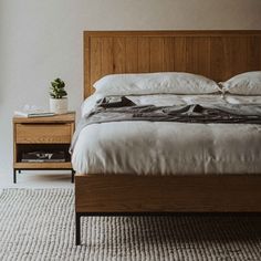 a bed with white linens and wooden headboard next to a window in a bedroom