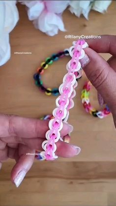 a person holding onto a pink and white bracelet on a wooden table with flowers in the background