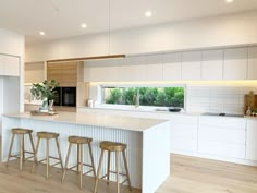 a large kitchen with white cabinets and counter tops, along with bar stools that match the hardwood flooring