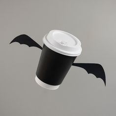 a paper cup with a black bat design on the lid is flying through the air