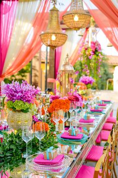 a table set up for a party with pink and orange flowers on the table cloth