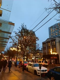 people are walking down the sidewalk in front of some buildings and cars at night time