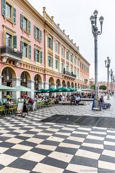 people are sitting at tables in the middle of a checkered floored area with tall buildings