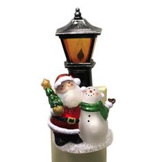 a glass christmas ornament with santa and snowmen on the base next to a street light