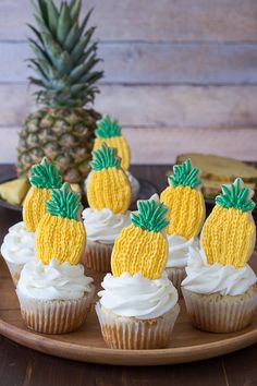 pineapple cupcakes with white frosting on a wooden plate next to bananas