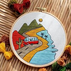 a cross stitch pattern with a red bus on the road and mountains in the background